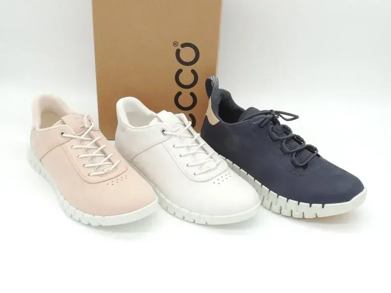 Drei ECCO-Sneaker in Beige, Weiß und Marineblau sind vor einem Karton ausgestellt.