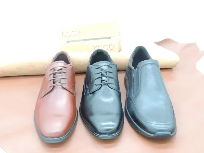 Drei Herrenschuhe in Braun, Schwarz und Blau auf hellem Hintergrund.