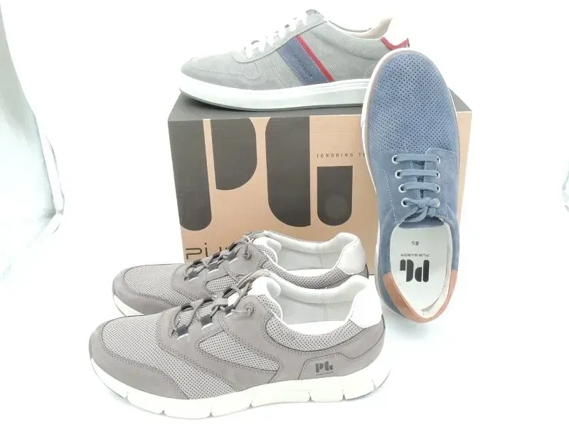 Graue und blaue Turnschuhe sind um einen Schuhkarton auf weißem Hintergrund angeordnet.