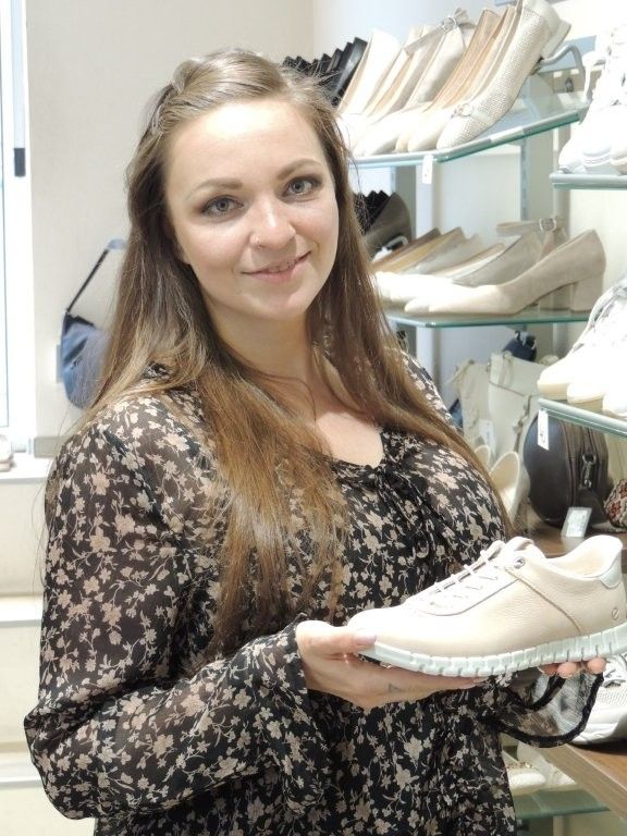 Eine Frau hält einen weißen Turnschuh in einem Schuhgeschäft, umgeben von Regalen voller Schuhe.