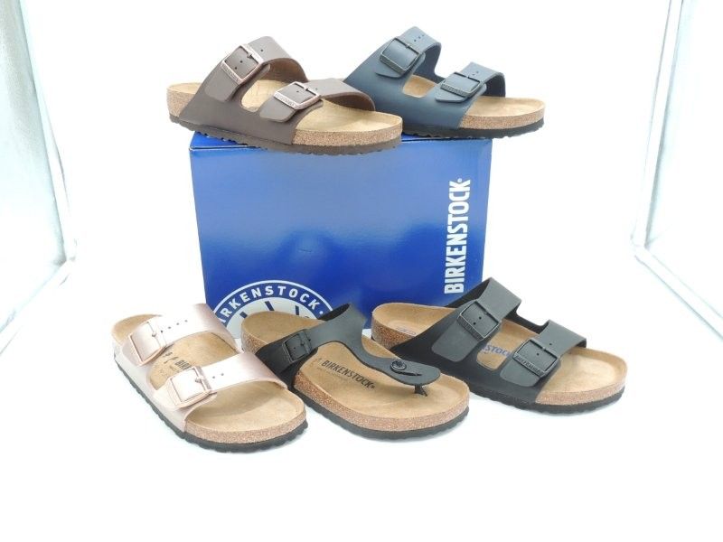 Sandalen in Braun-, Blau- und Weißtönen, präsentiert auf einer blauen Schachtel.