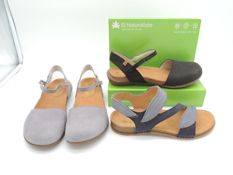 Zwei Paar Damensandalen, grau und blau, vor einem grünen Schuhkarton-Hintergrund