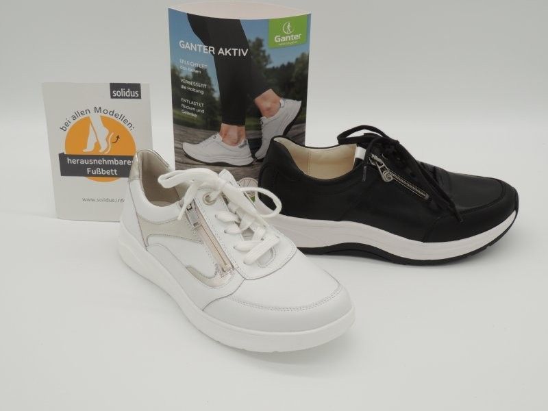 Weiße und schwarze Sportschuhe werden zusammen mit der Produktverpackung auf einem einfarbigen Hintergrund präsentiert.