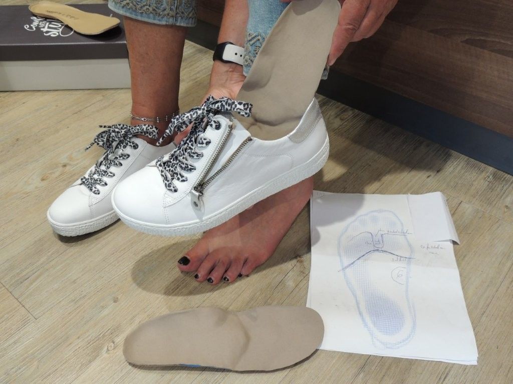 Eine Person passt weiße Schuhe mithilfe einer Fußschablone und eines Papiermusters auf dem Boden an.