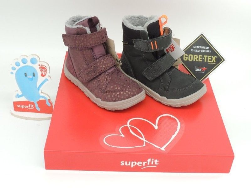 Ein Paar Kinderwinterstiefel auf einem roten Superfit-Karton, ein lila und ein schwarzer Stiefel mit GORE-TEX-Etikett.