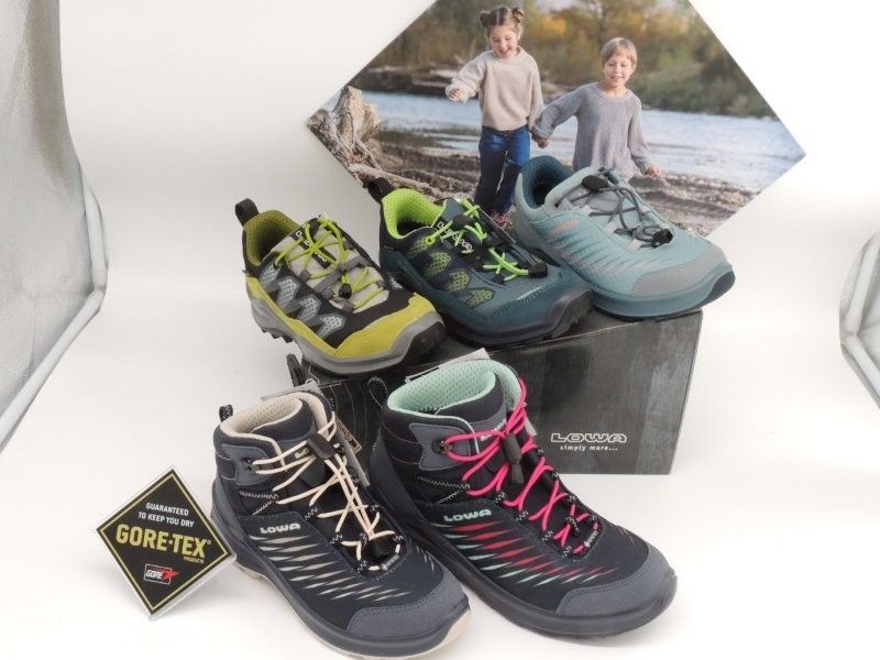 Verschiedene Wanderschuhe und -stiefel mit Gore-Tex-Etikett und Fotohintergrund im Freien ausgestellt.