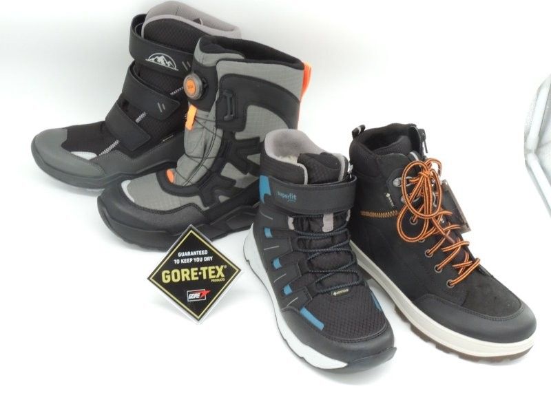 Drei schwarze und graue Wanderschuhe mit orangefarbenen Schnürsenkeln und einem Gore-Tex-Etikett auf weißem Hintergrund