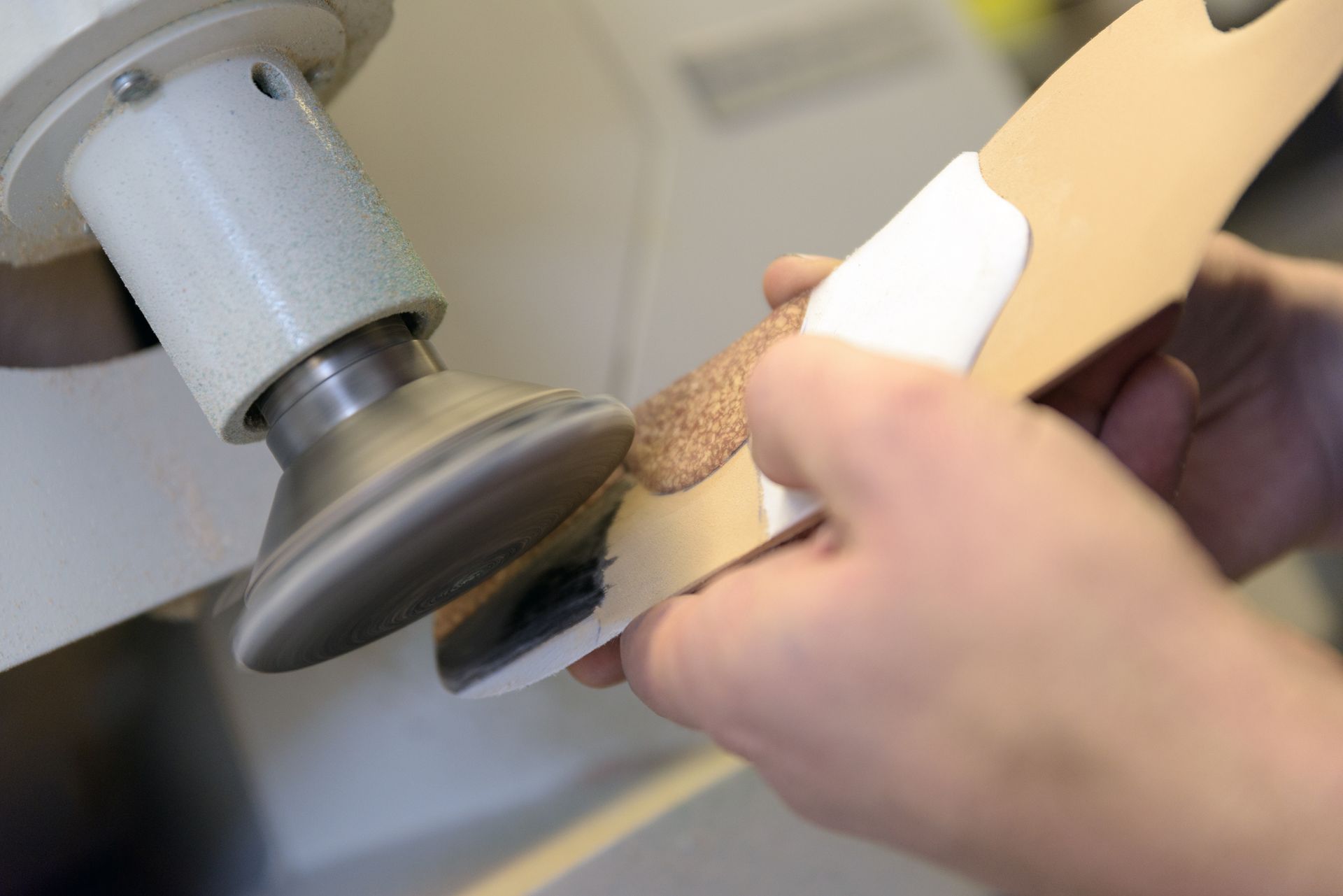 Hände, die mit einem Schleifwerkzeug ein Holzobjekt auf einer Werkbank glätten.