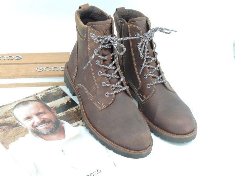 Braune Schnürstiefel neben einem Foto eines lächelnden Mannes vor weißem Hintergrund