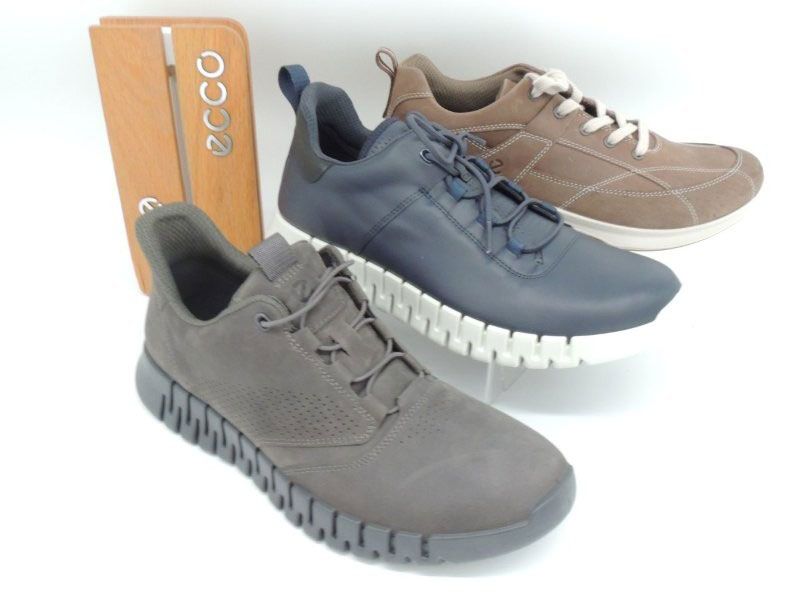 Drei ECCO-Sneaker in Grau, Marineblau und Taupe neben einem orangefarbenen Schuhkarton