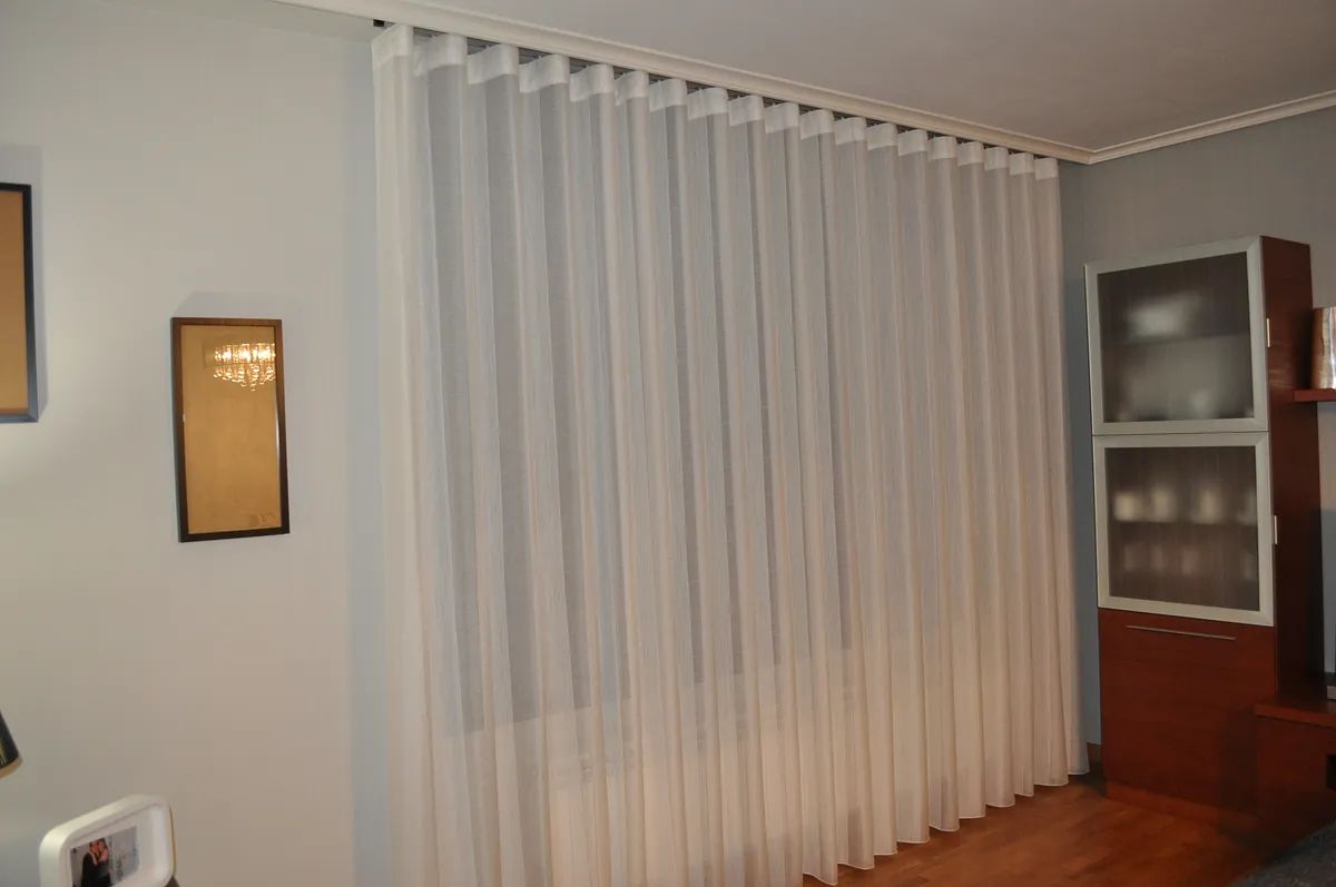 Una sala de estar con cortinas blancas y suelo de madera.