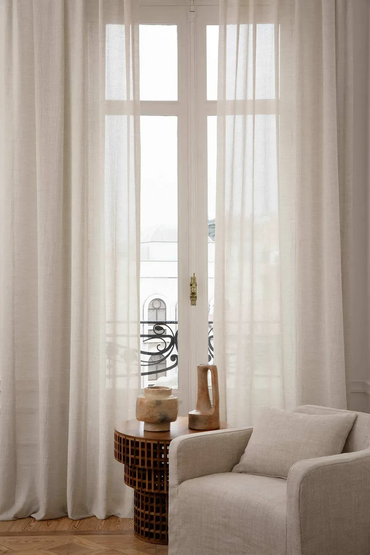 Una sala de estar con una silla y una mesa frente a una ventana con cortinas blancas.