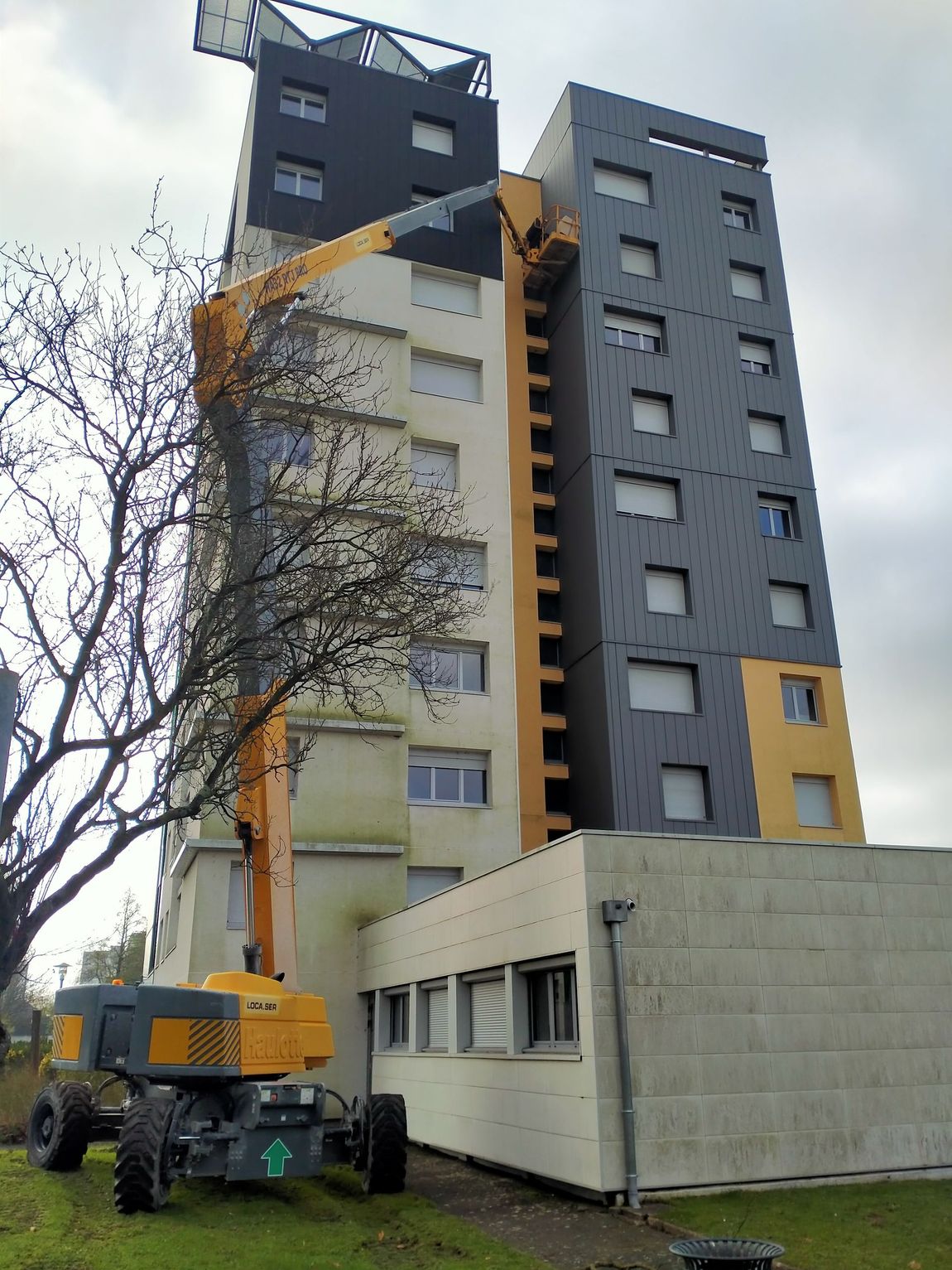Photos d'un immeuble gris avec une grue jaune devant
