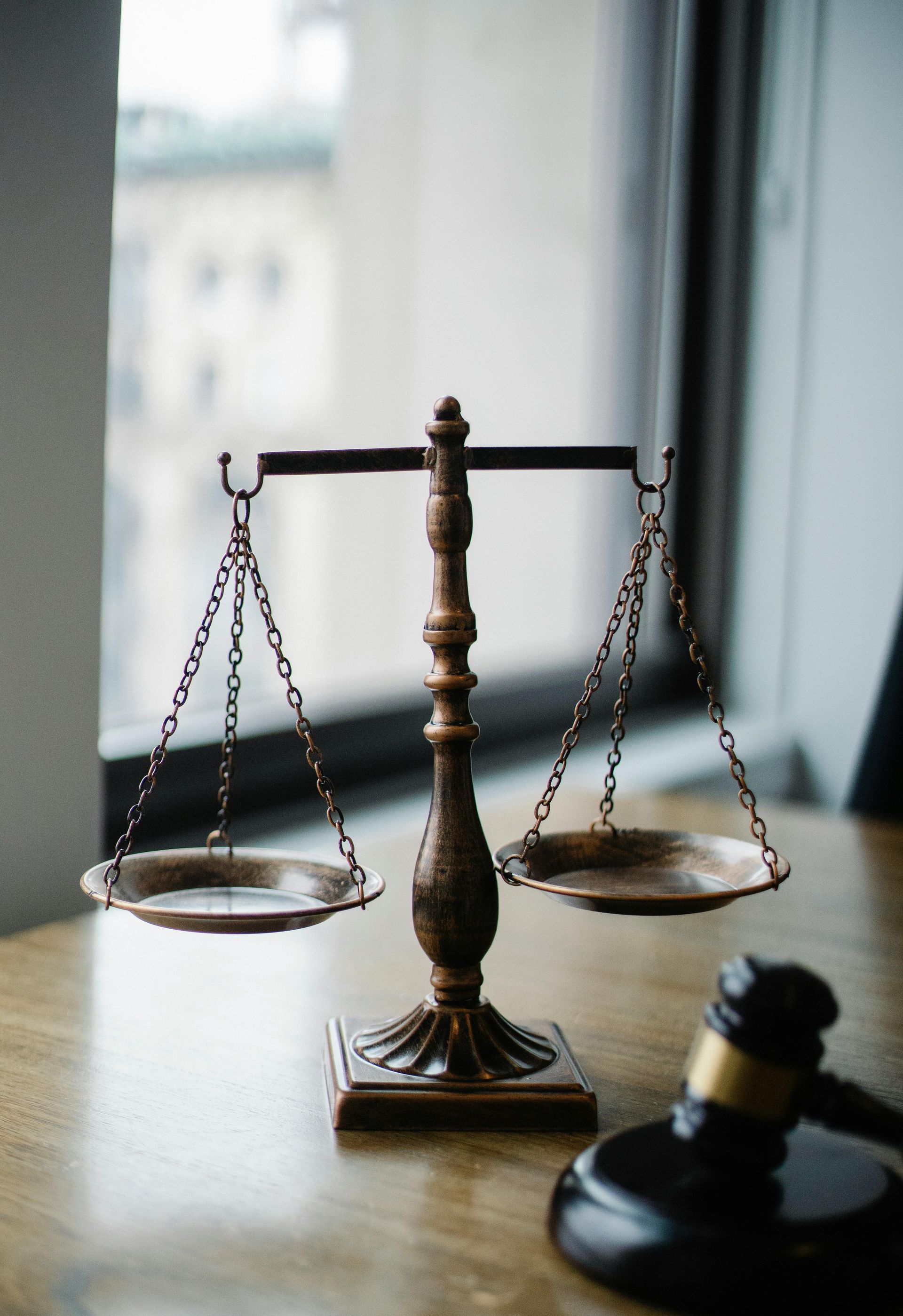 Balanza de la justicia y un mazo sobre una mesa de madera cerca de una ventana.