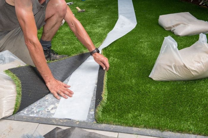 Un hombre está instalando césped artificial en un patio.