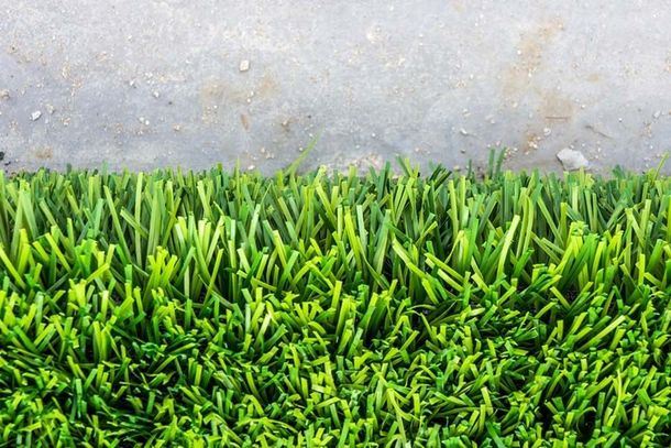 Un primer plano de un trozo de césped verde junto a una superficie de hormigón.