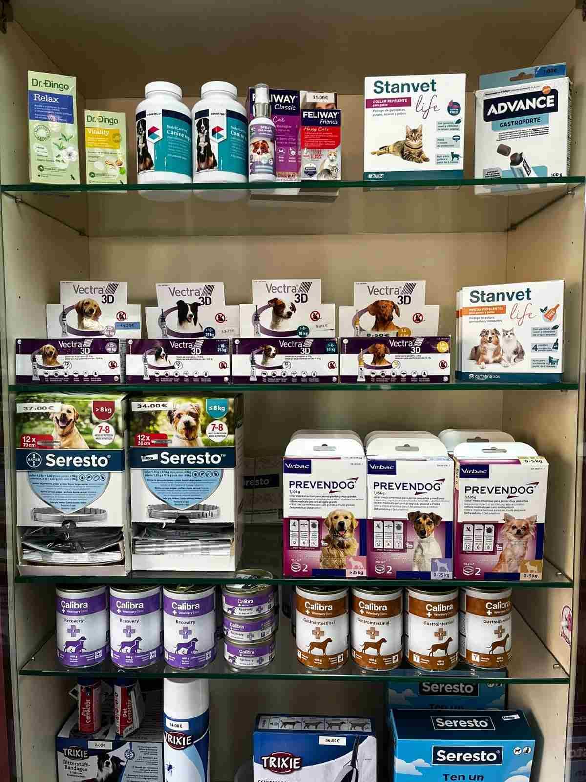 Estanterías con productos y botellas para el cuidado de mascotas en un pasillo de una tienda, con un transportín para mascotas a la derecha.