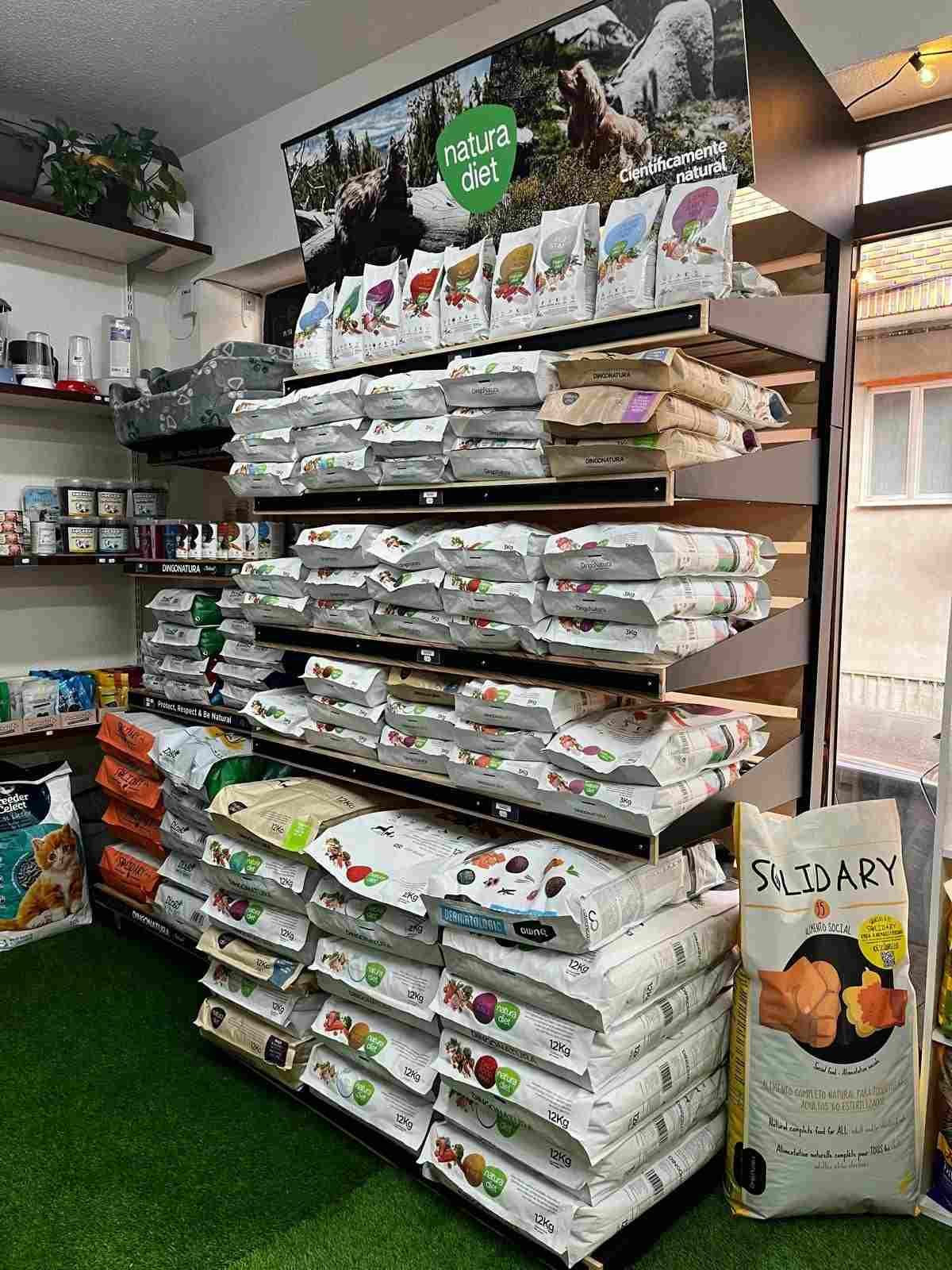Bolsas de comida para mascotas apiladas en los estantes de una tienda cerca de una ventana y macetas.
