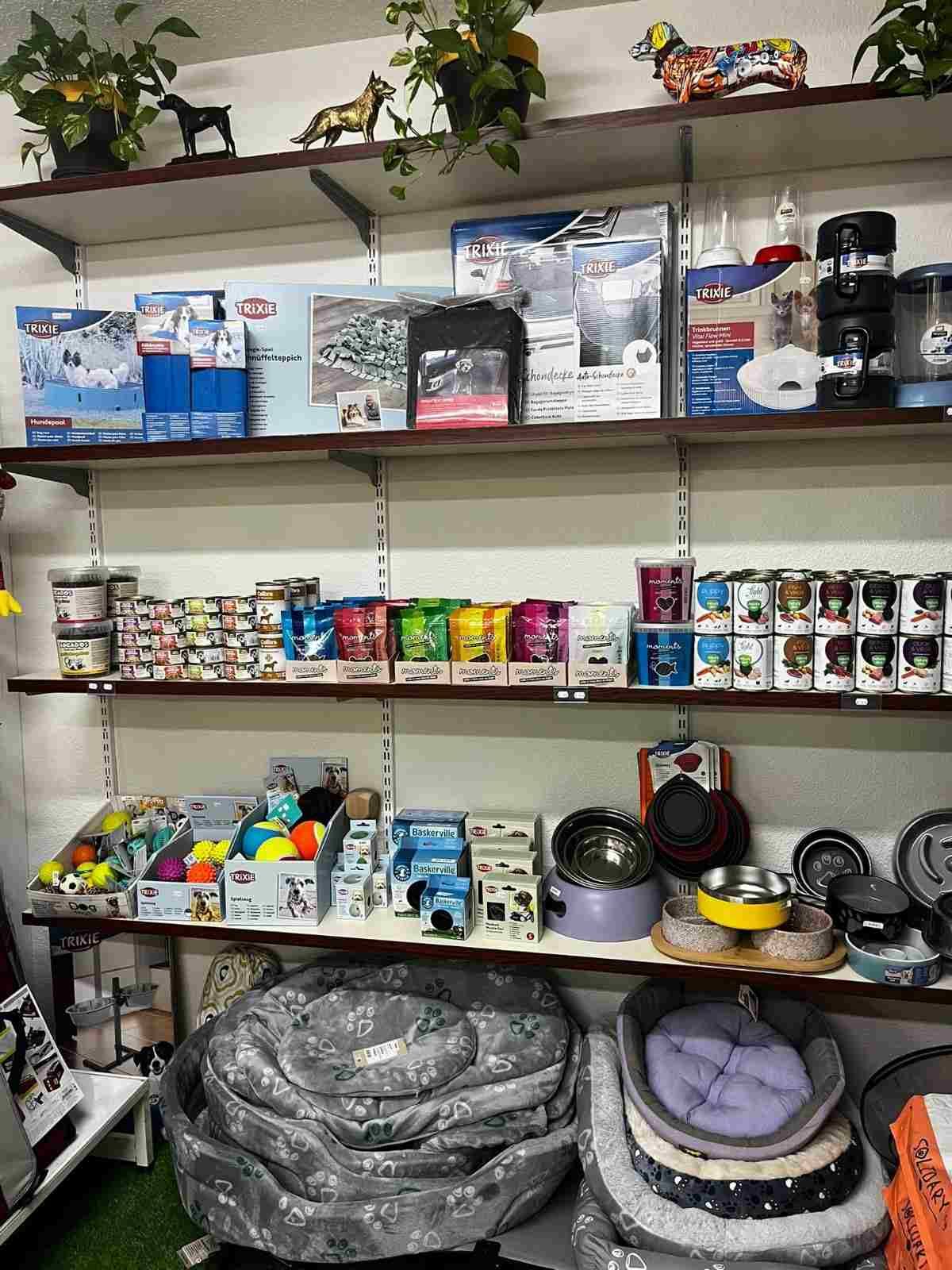 Estanterías repletas de artículos variados para mascotas, latas de comida, cajas de arena y camas para mascotas apiladas en un pasillo de la tienda.