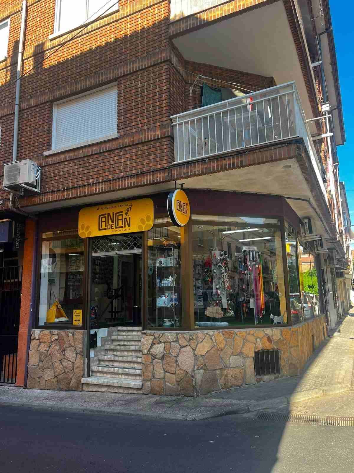 Local comercial en esquina con base de piedra, ventanas de cristal, toldo amarillo y un pequeño balcón en la parte superior.