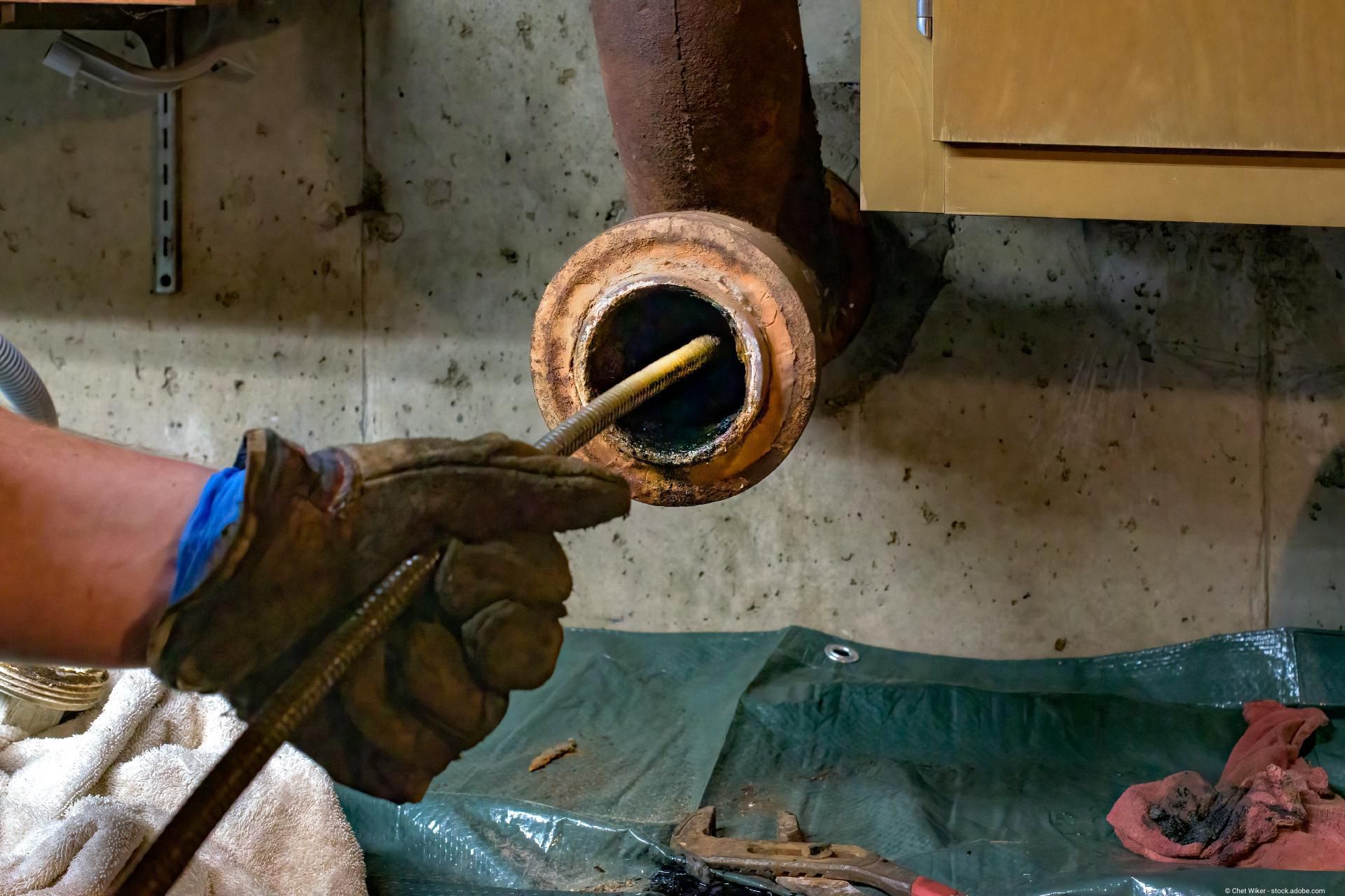 Mechanische Rohrreinigung: Handwerker führt eine Reinigungsspirale in ein verstopftes Abflussrohr ein.