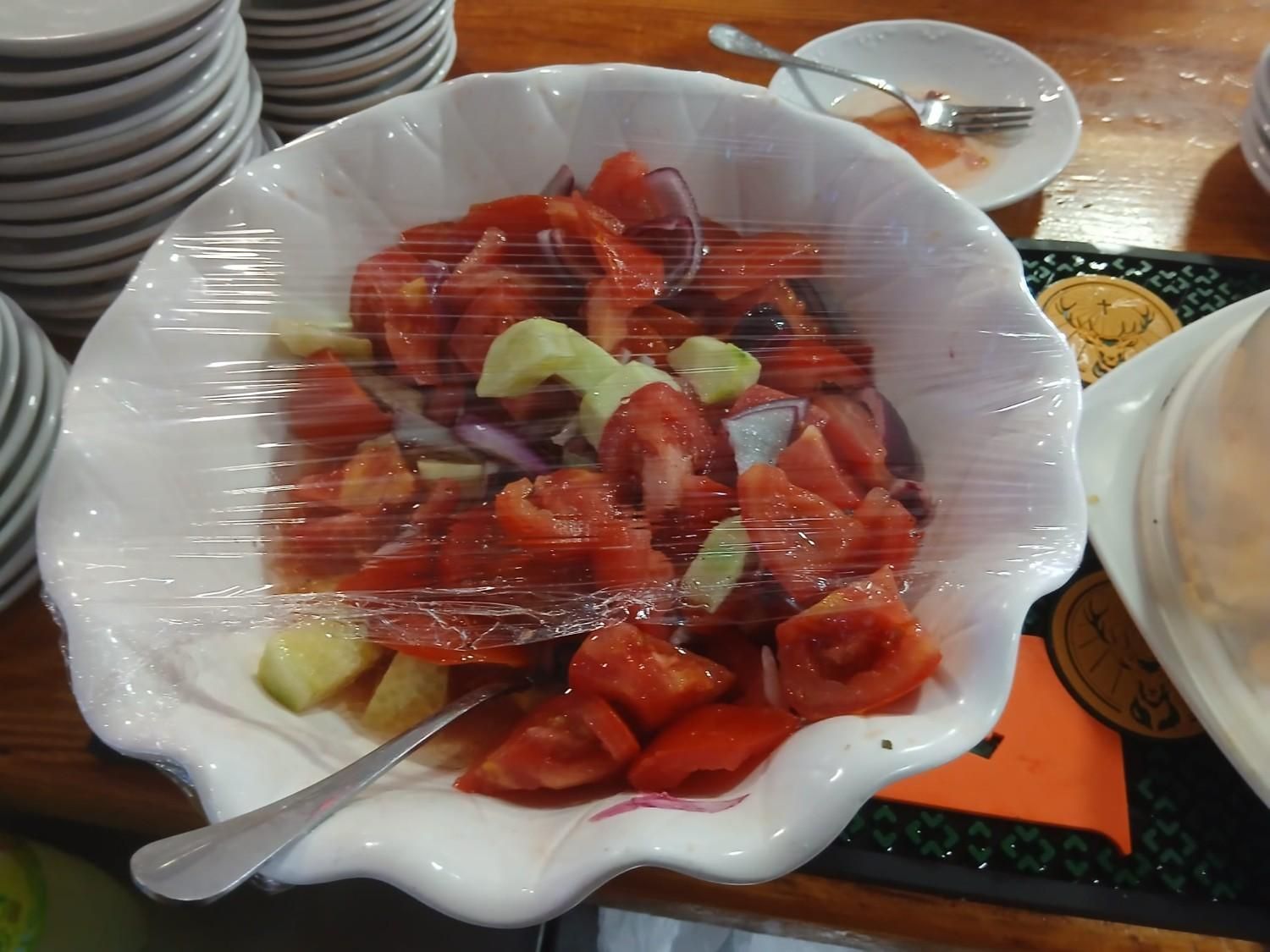 Un bol de ensalada de fresas envuelto en plástico sobre una mesa con una cuchara.