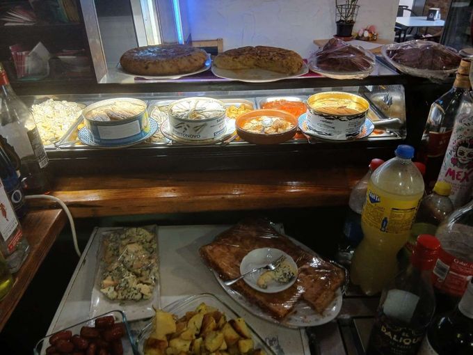 Mesa de buffet con platos cubiertos, ensaladas, pasteles y bebidas en un entorno de restaurante.