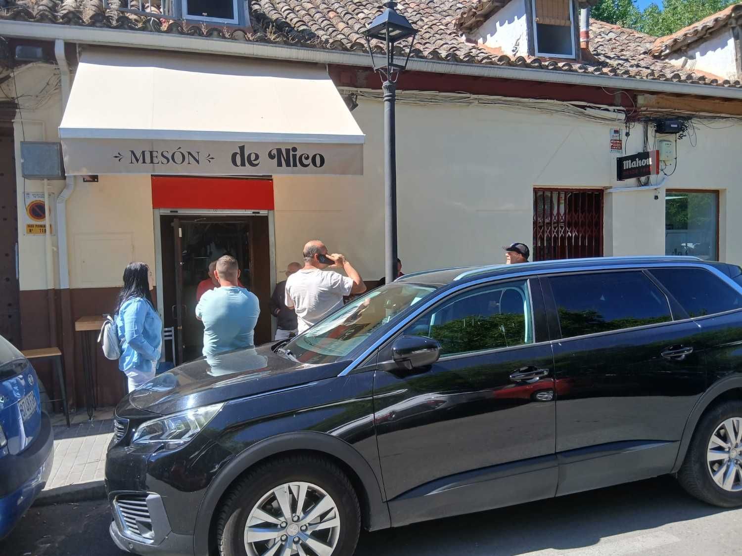 Varias personas se congregaron frente a un pequeño edificio de oficinas; un SUV negro estaba estacionado delante.