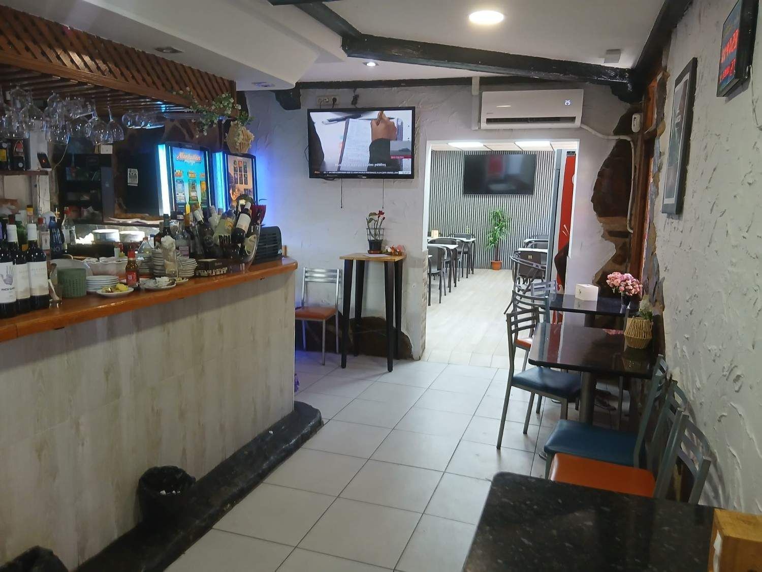 Interior vacío de un restaurante con barra, televisor de pared, mesas, suelo de baldosas