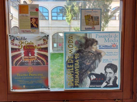 Escaparate con carteles anunciando un desfile de moda y un evento de gala en un patio.