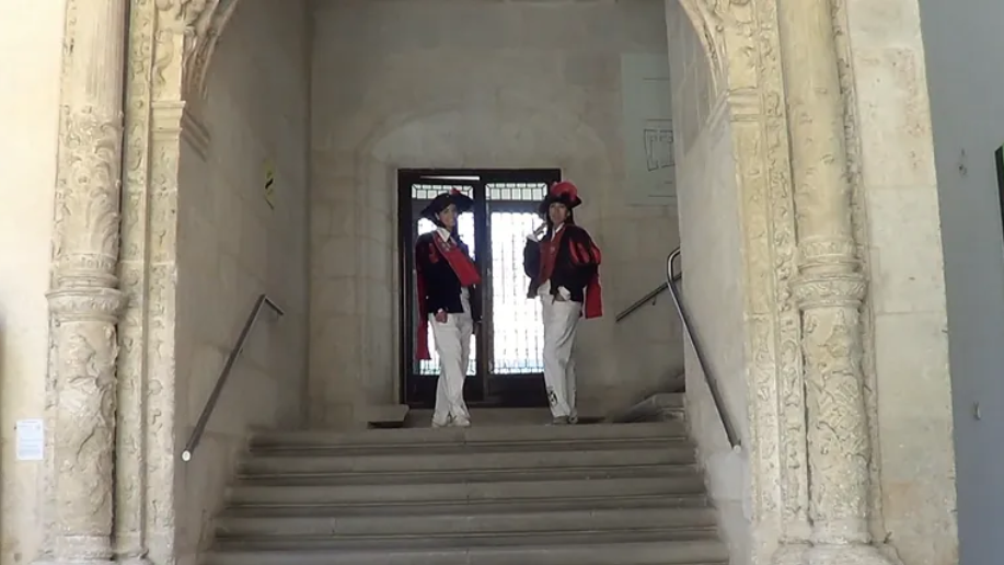Dos personas con atuendos históricos en las escaleras de una puerta de piedra.