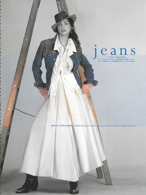 Mujer con chaqueta vaquera, vestido blanco y sombrero de vaquero posa junto a una escalera.