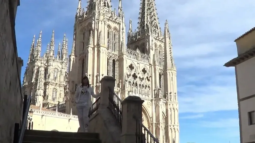 Mujer desciende escalones de piedra, Catedral de Burgos al fondo, día soleado.