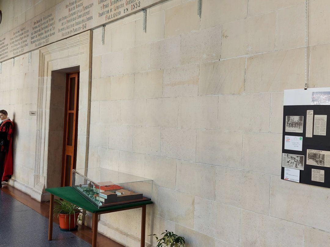 Un pasillo de piedra con una puerta de madera, una mesa con una maqueta y un tablero de exposición; una persona está de pie junto a la puerta.