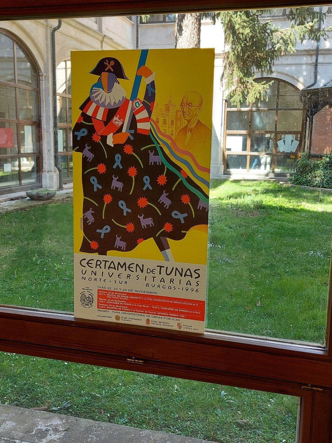 Cartel para concurso de atún; figura colorida sosteniendo un bastón, fondo amarillo, exhibido cerca de un patio con césped.