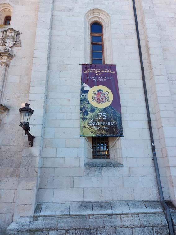 Una pancarta sobre un edificio de piedra blanca celebra sus 175 años. Incluye un escudo de armas y una escena natural.