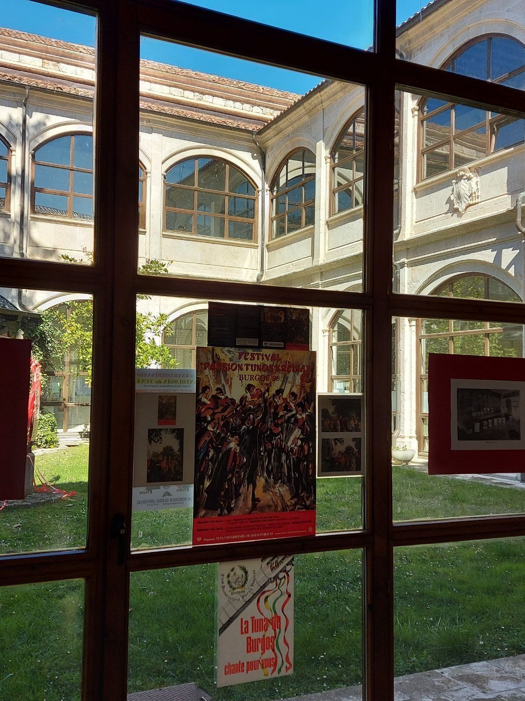 Vista a través de una ventana a un patio abierto con carteles y un edificio blanco.