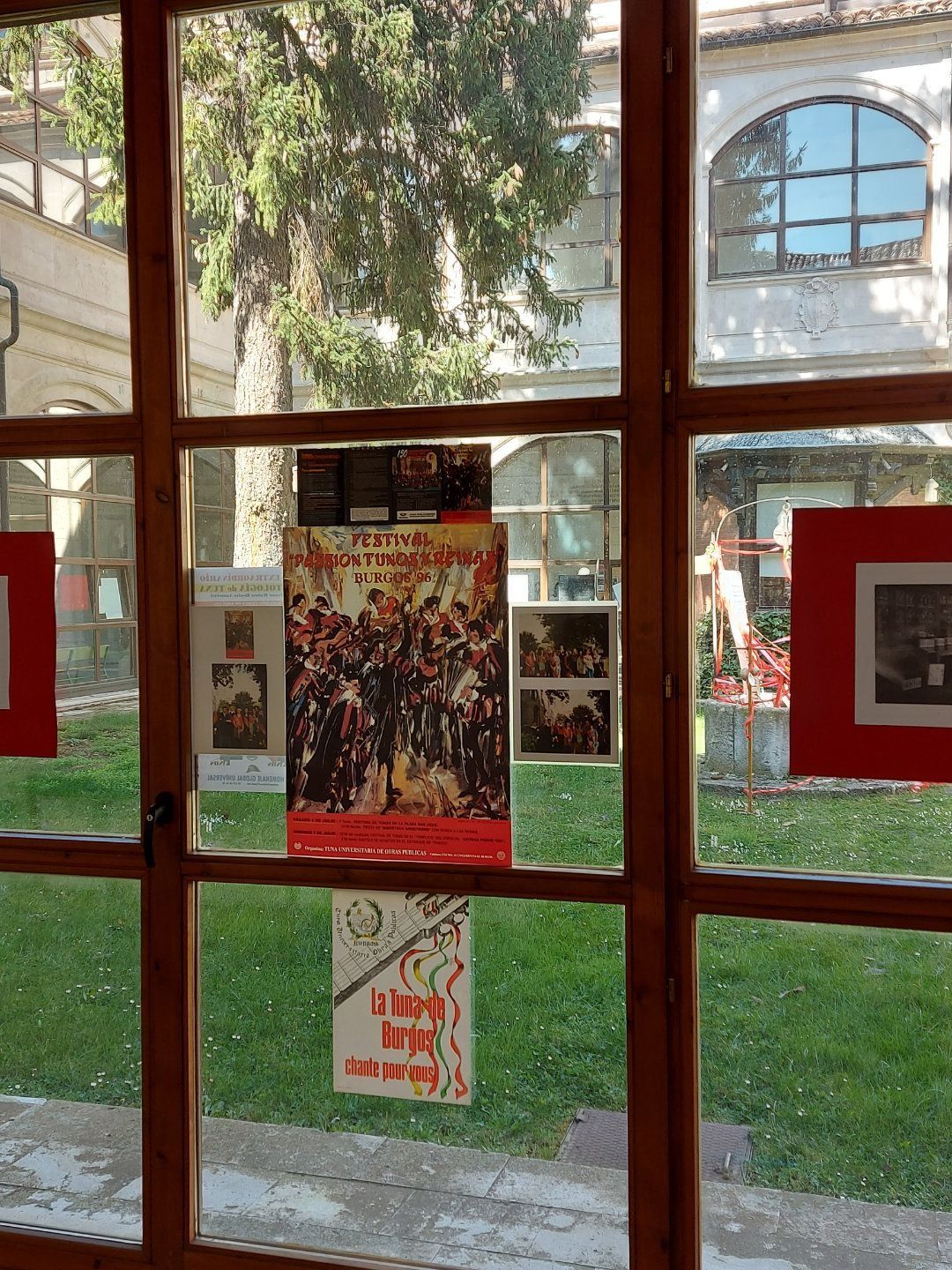 Ventana con carteles exhibidos, detalles en rojo y vista exterior del edificio y el césped.