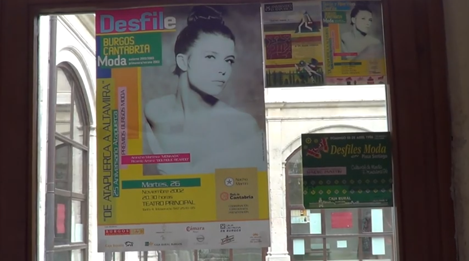 Cartel de un desfile de moda con el retrato de una mujer en una ventana. También se ven otros carteles promocionales.