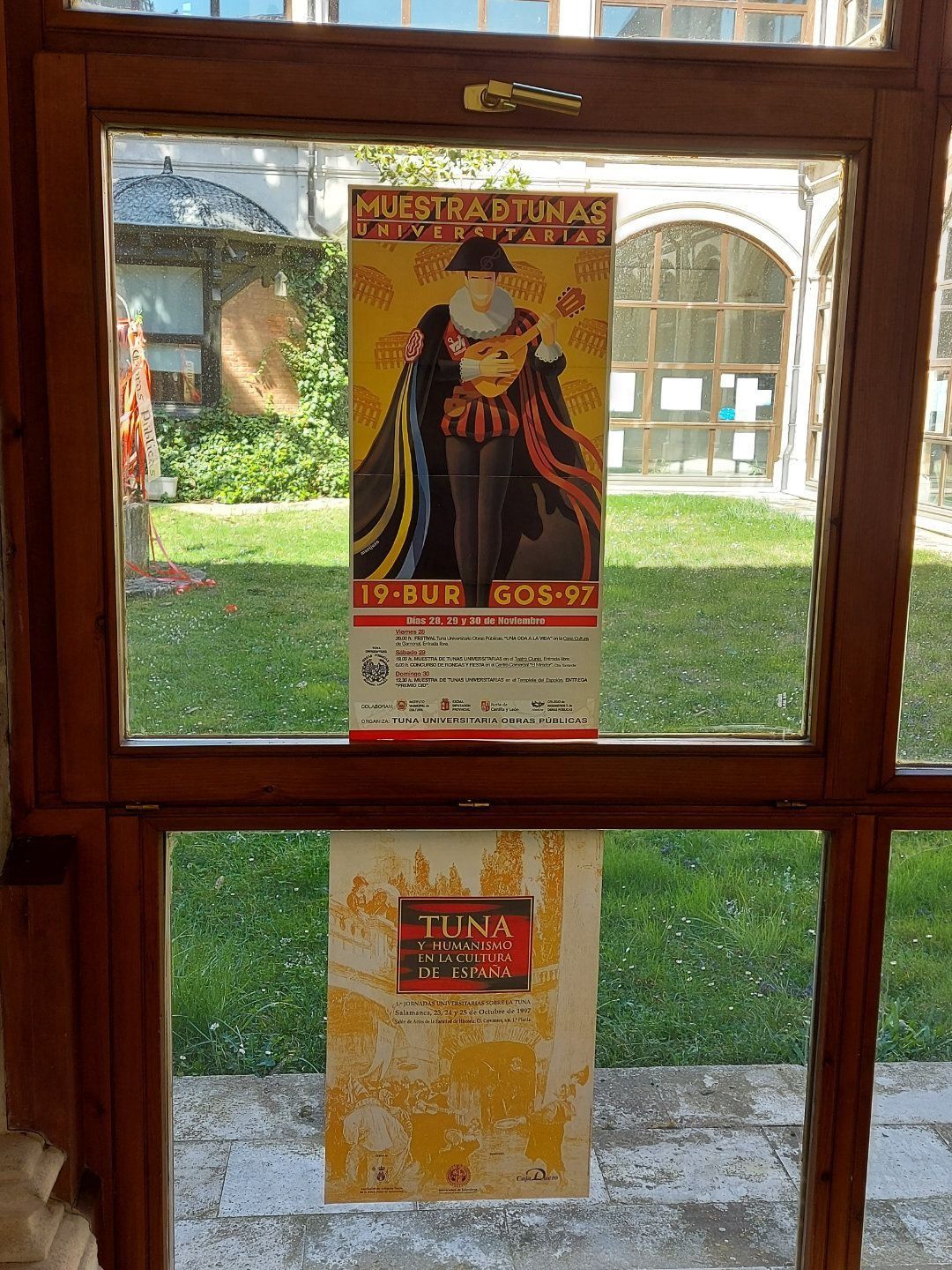 Dos carteles en el marco de una ventana. Uno muestra a un hombre con ropa de época; el otro, descolorido, presenta un diseño dorado.