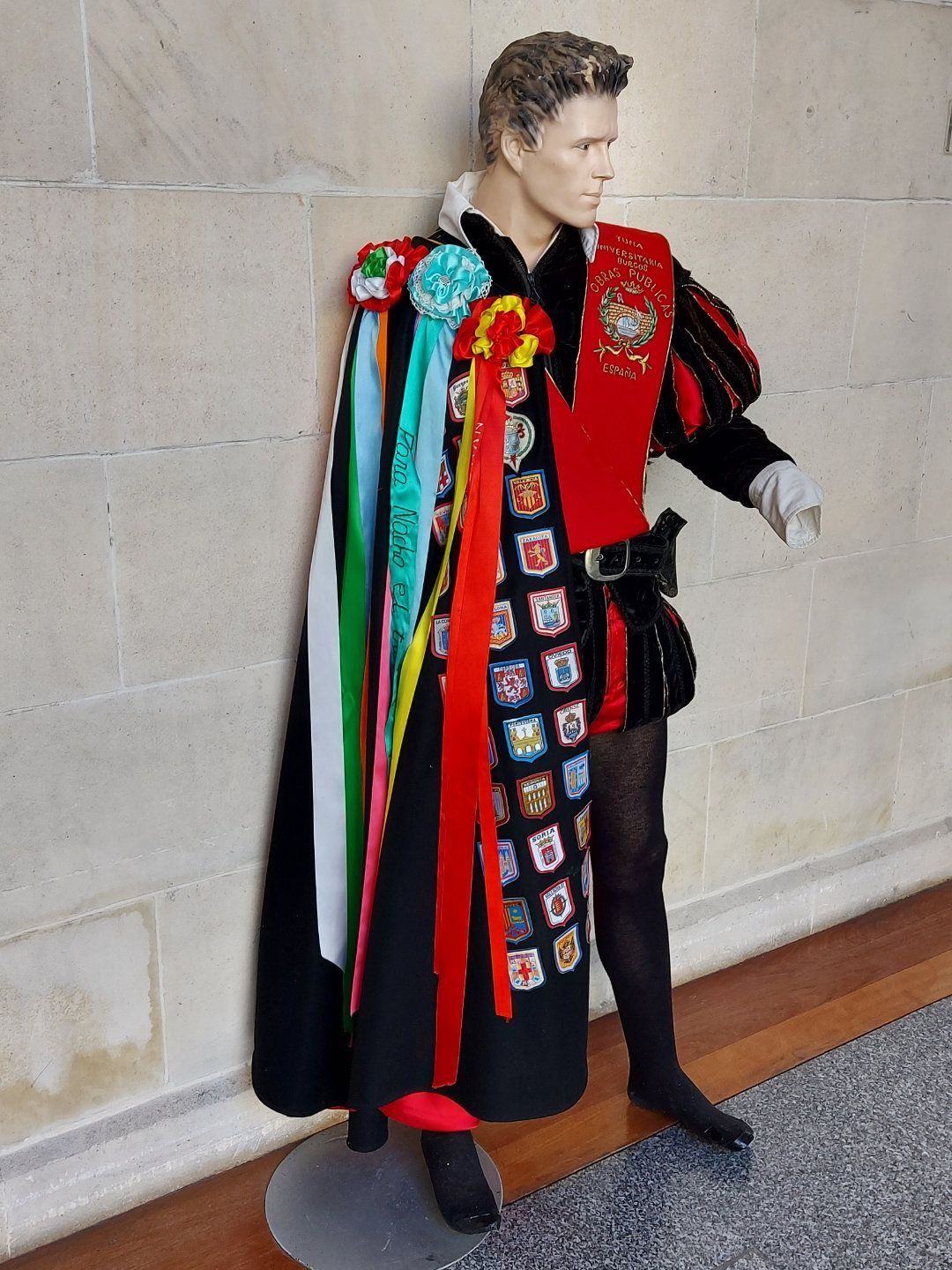 Maniquí con atuendo ornamentado de color rojo y negro, capa con cintas e insignias.
