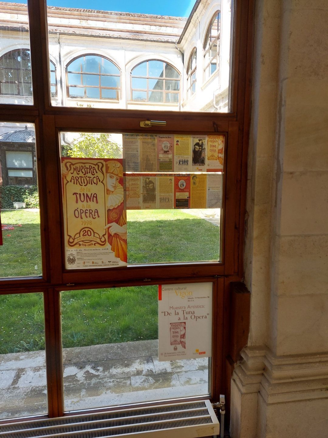 Vista de un patio a través de una ventana con carteles, un marco de madera y una pared blanca.