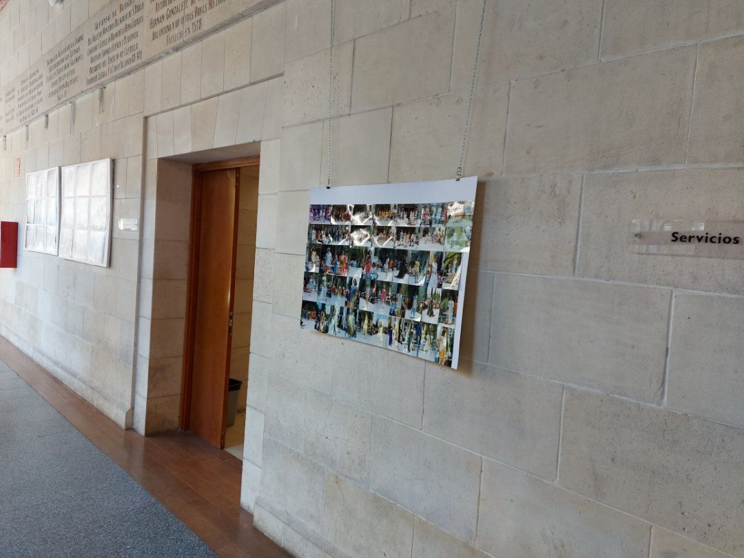 Pasillo con paredes de piedra. Una exposición de fotografías a la derecha. Una puerta de madera en el centro y un cartel que dice 
