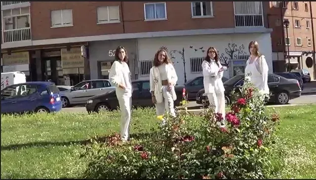 Cuatro mujeres vestidas de blanco posan cerca de rosales, fondo urbano.