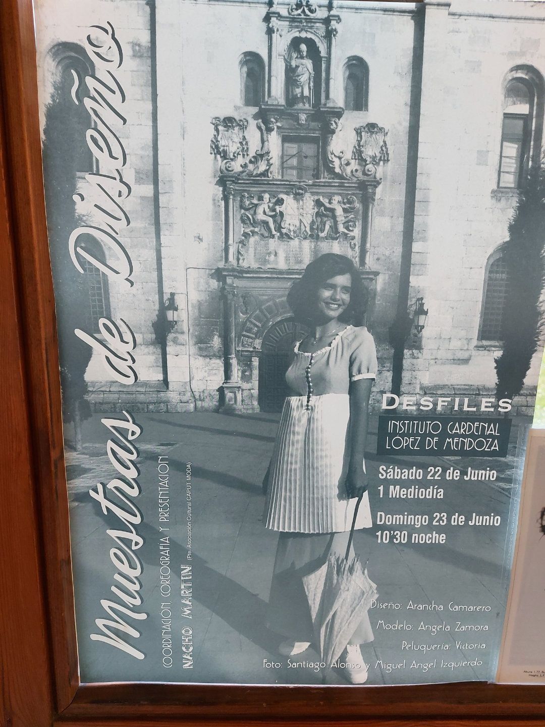 Cartel de un desfile de diseño de moda. Una mujer sostiene un paraguas frente a un edificio. Texto: 