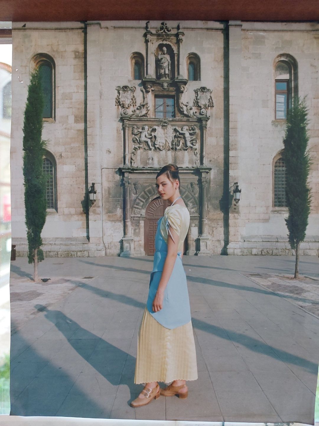 Mujer con vestido vintage posa frente a un edificio de piedra con fachada ornamentada.