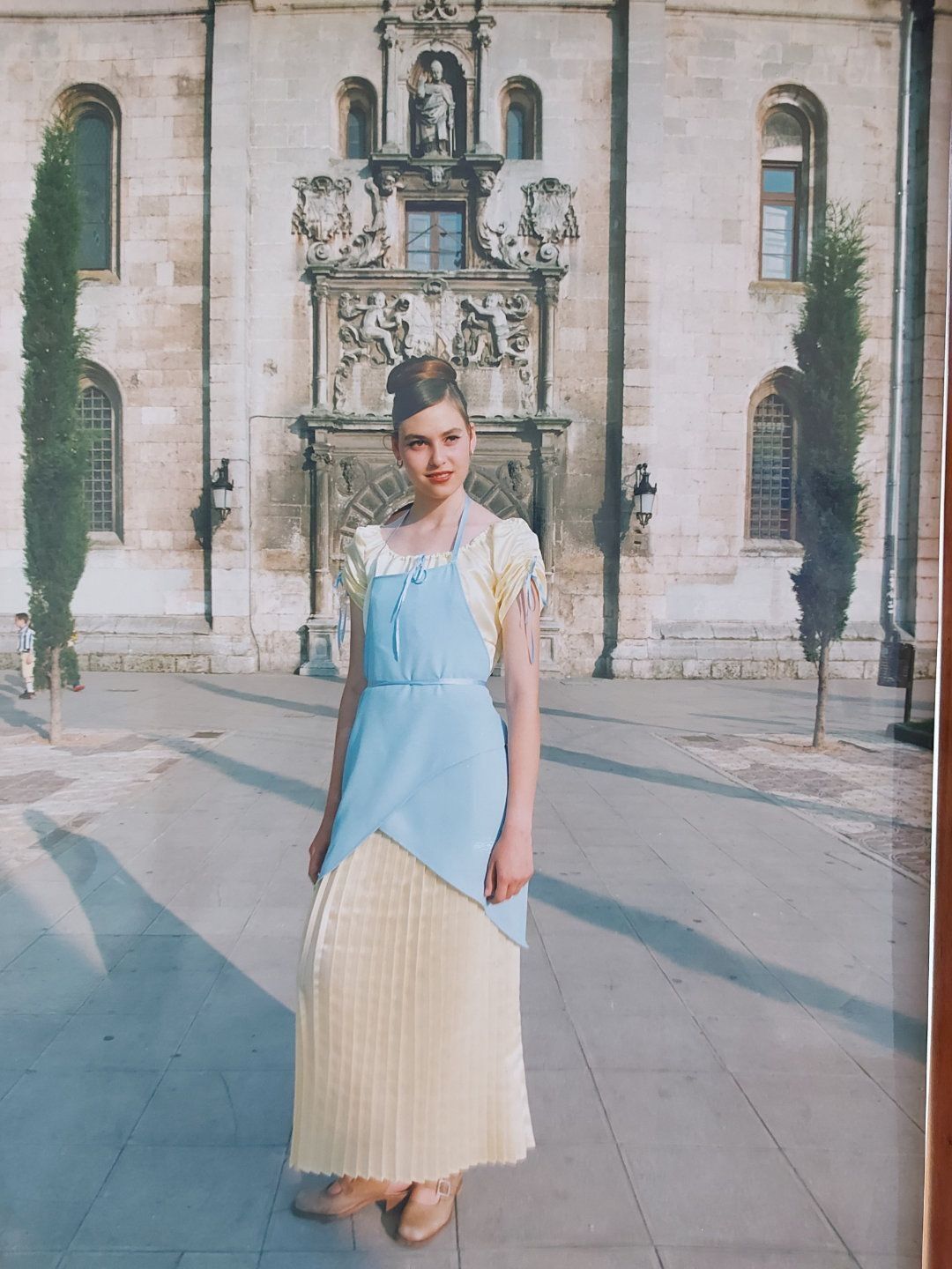 Una mujer disfrazada de Cenicienta se encuentra frente a un edificio de piedra con tallas intrincadas.