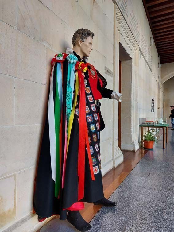 Maniquí con traje formal, con cintas de colores, de pie en un pasillo.