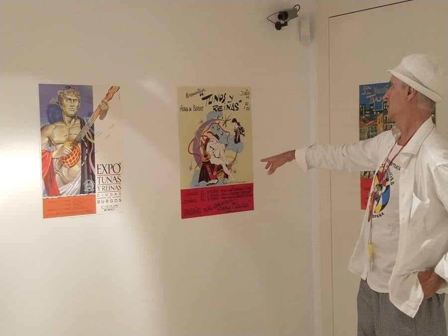 Un hombre con sombrero blanco señala carteles coloridos en la pared de una galería.