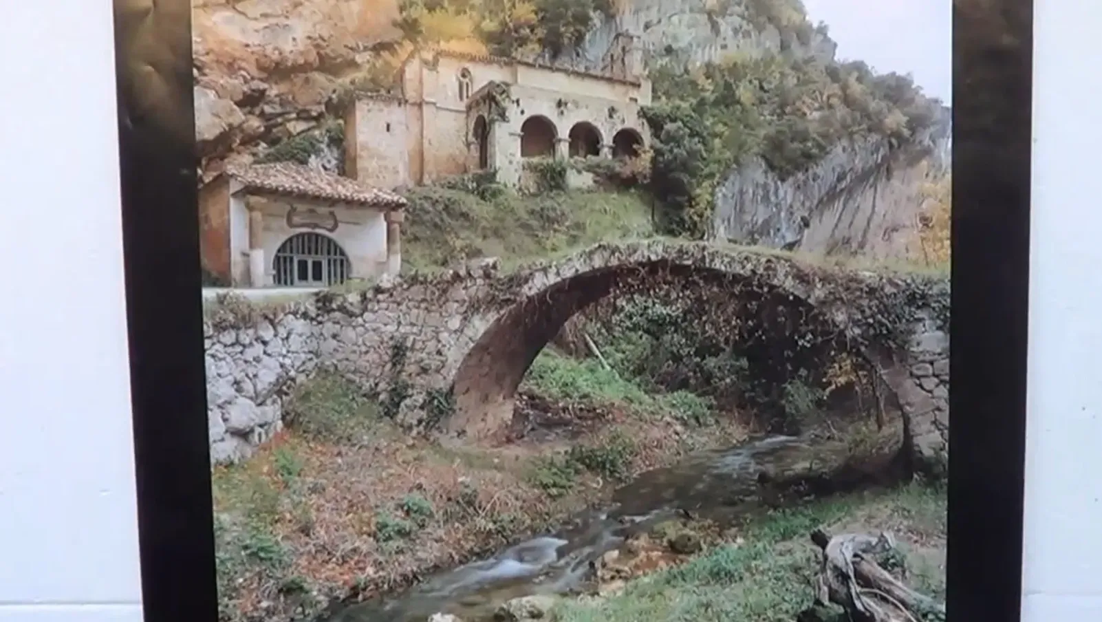 Puente de piedra sobre arroyo con edificio al fondo.